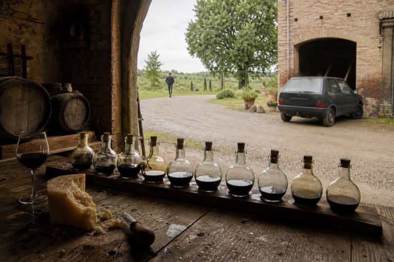 Dark balsamic drops on a wooden board with broken Parmigiano and a glass of Lambrusco in a brick cellar near Modena