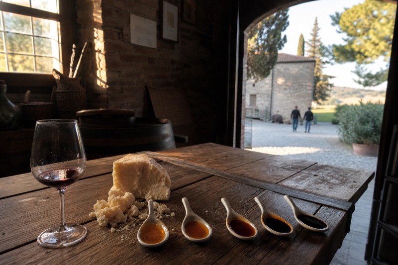 Five spoons of balsamic from amber to near-black beside crumbled Parmigiano and Lambrusco in a Modena hillside cellar
