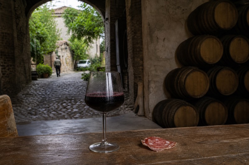 A glass of frizzante Lambrusco with condensation beside a curled slice of salami in Castelvetro di Modena cellars