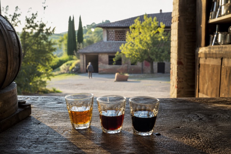 Three glasses of balsamic vinegar from amber to black on an oak table in Castelvetro di Modena