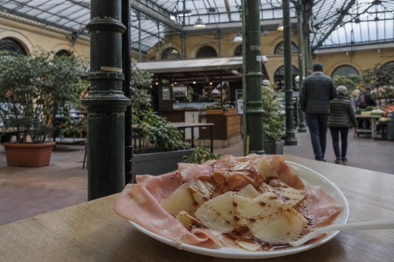 Mortadella and shaved Parmigiano with balsamic on a small plate under the glass roof of Modena's Mercato Albinelli