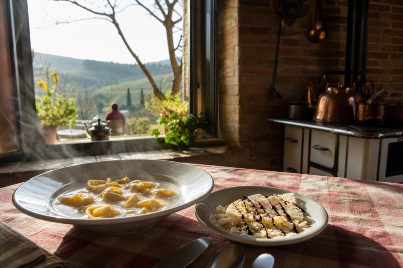 A steaming bowl of tortellini in brodo on a checked tablecloth in a Vignola farmhouse kitchen
