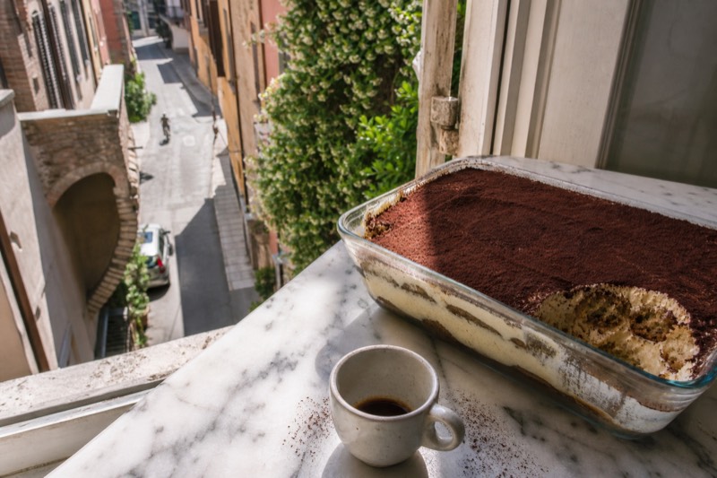 A glass dish of tiramisu with an espresso cup on a marble table in a Modena apartment