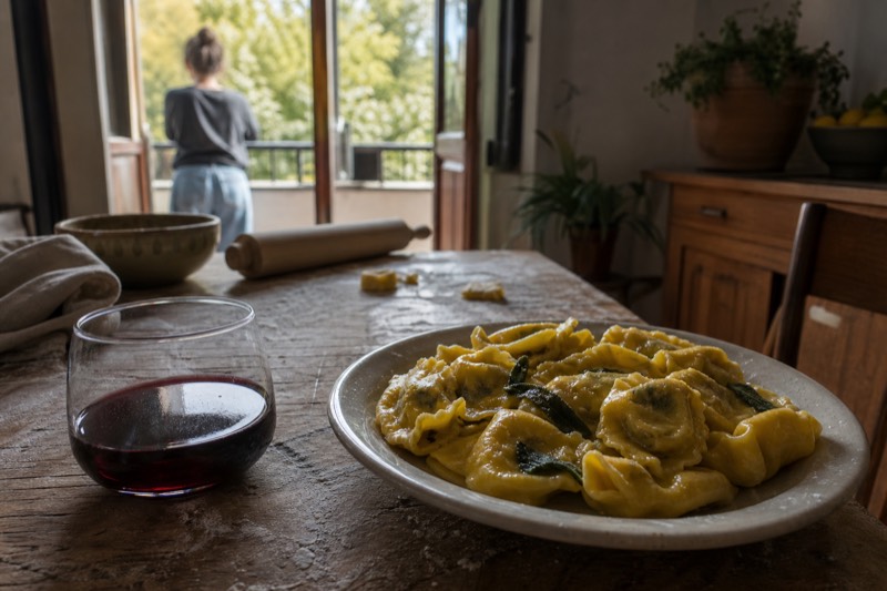Hand-rolled tortelloni with butter and sage on a flour-dusted board beside a glass of Lambrusco in a Modena kitchen