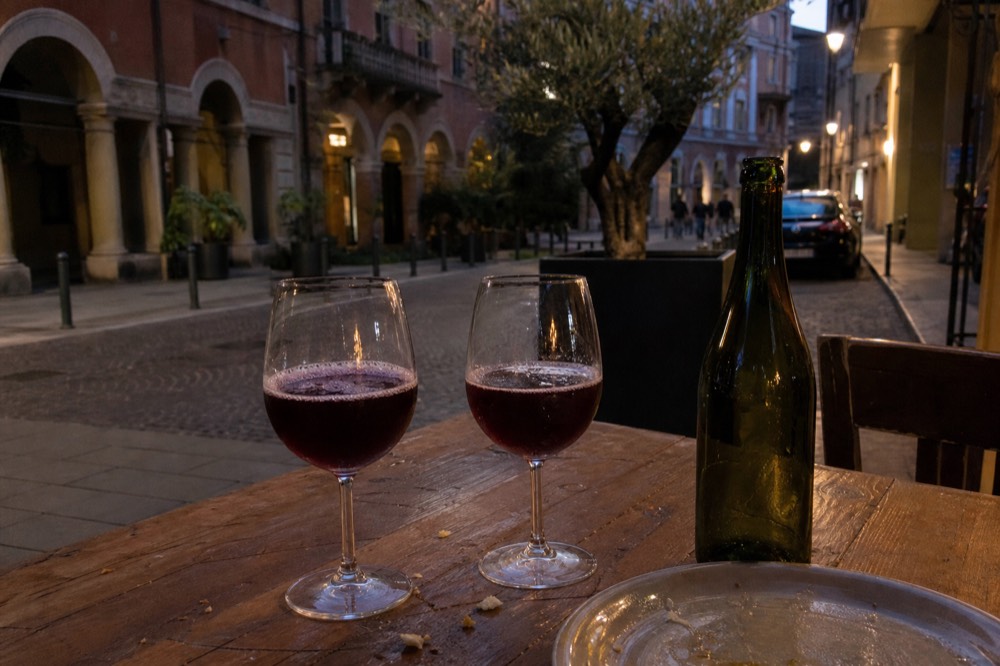 Two stemmed glasses of dark sparkling red wine on a rustic table beside an open bottle
