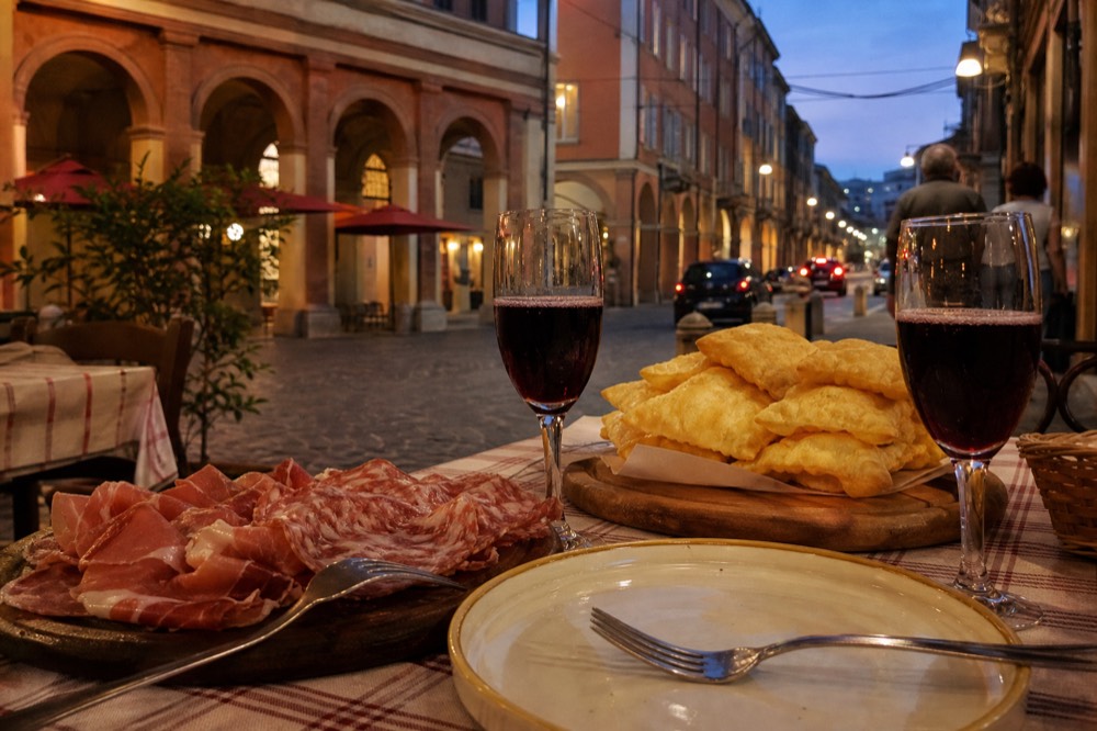 A table of cured meats, fried dough and two glasses of sparkling red wine in a Modena trattoria