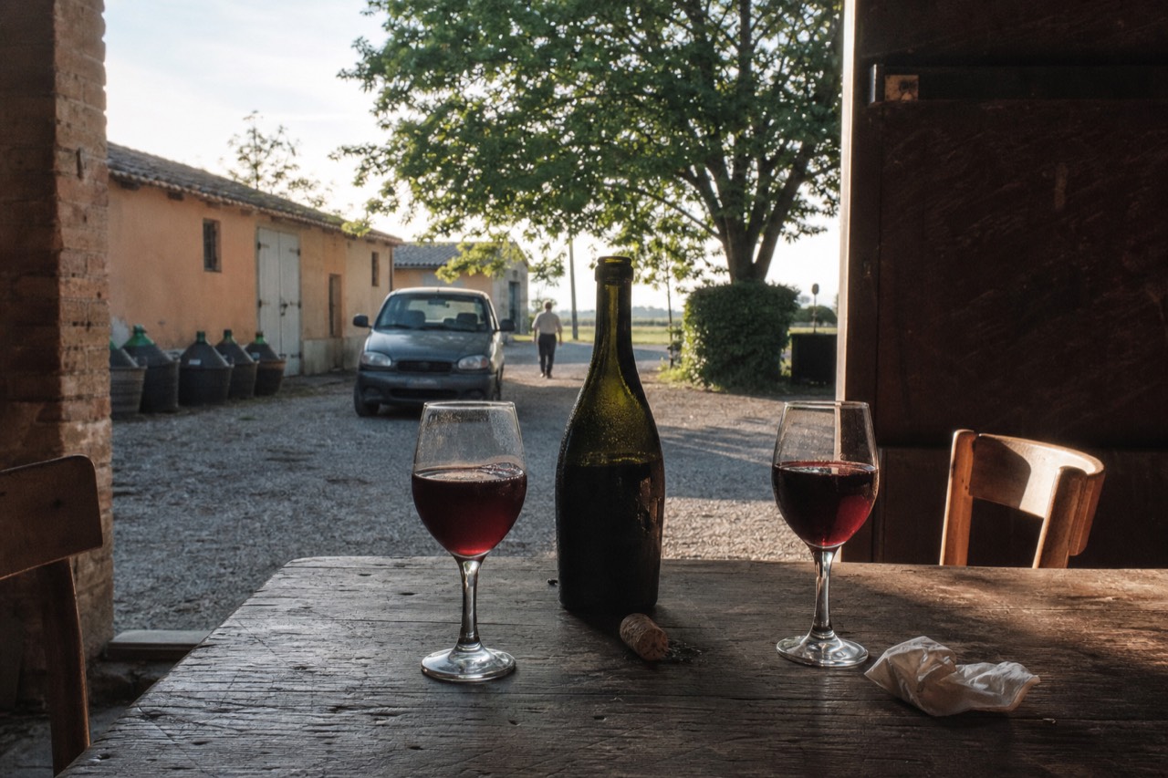 A chilled bottle of Lambrusco and two stemmed glasses on a wooden table in an Emilian cellar
