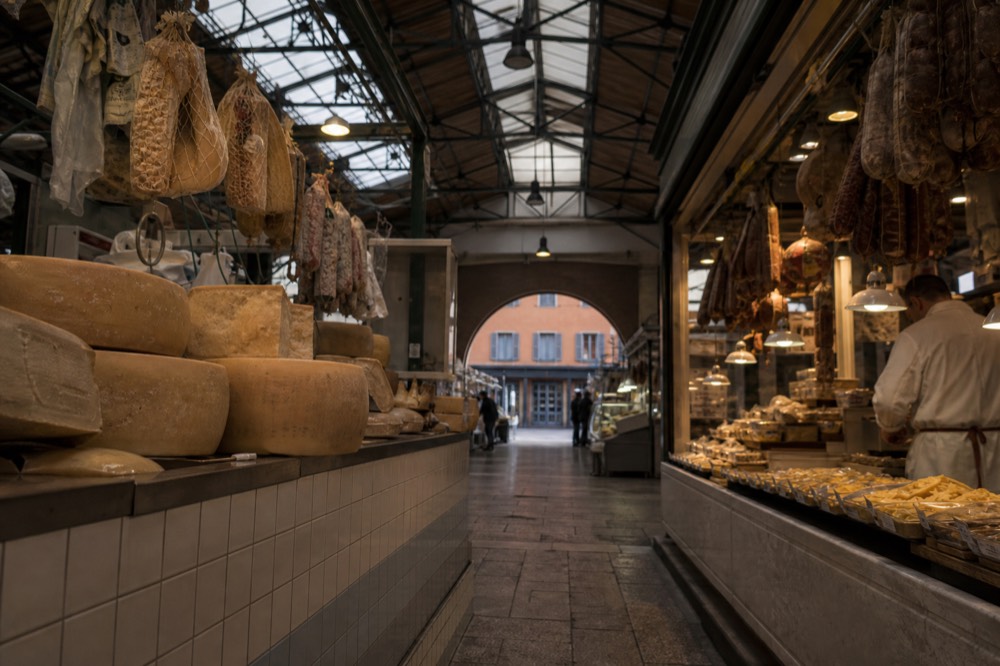 A covered market hall with stalls of cheese, cured meats and fresh pasta under warm lights