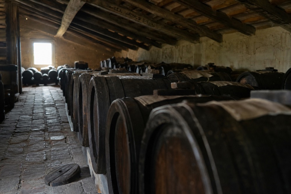 Rows of small wooden ageing barrels in a dim attic loft with a window at the end