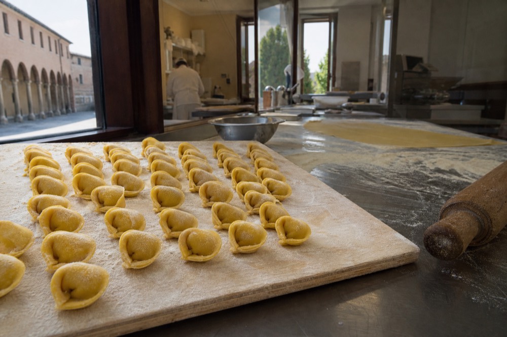A wooden pasta board with fresh tortellini arranged in rows, flour dusted across the surface