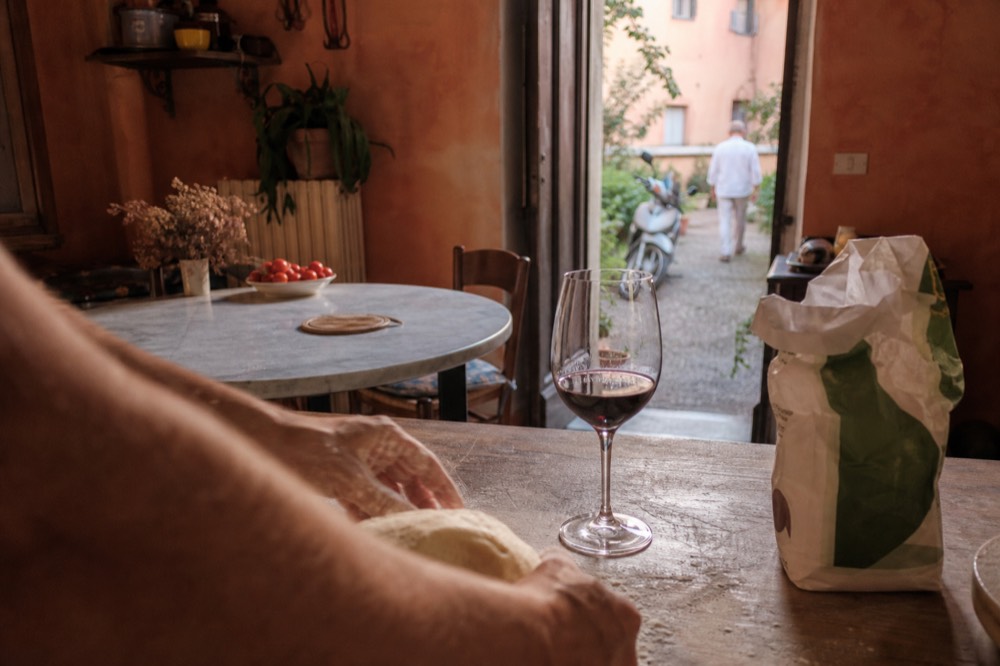 A cook's hands kneading fresh pasta dough on a floured wooden surface in a Modena kitchen