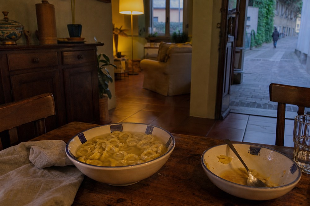 A completed plate of tortellini in brodo on a rustic table, steam rising from the bowl in a Modena home