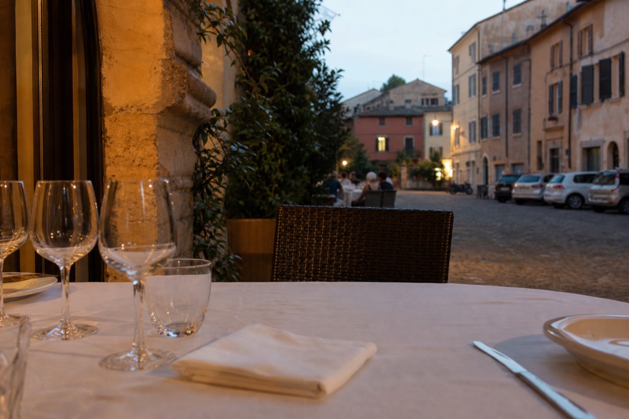 A set dining table with white linen and wine glasses in a softly lit Modena dining room