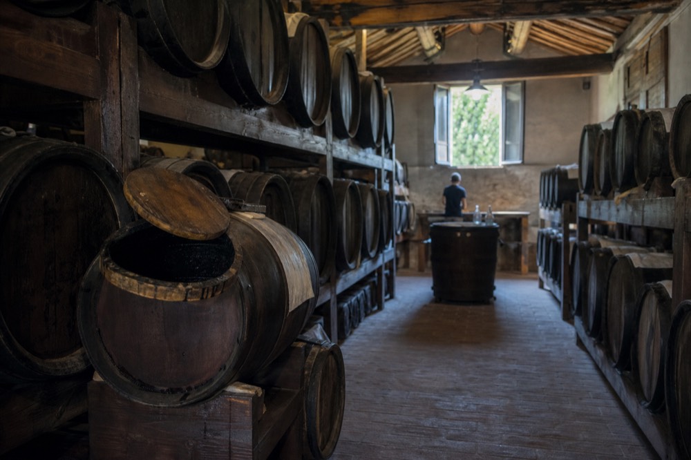Small wooden barrels stacked in rows inside a dim balsamic vinegar ageing loft