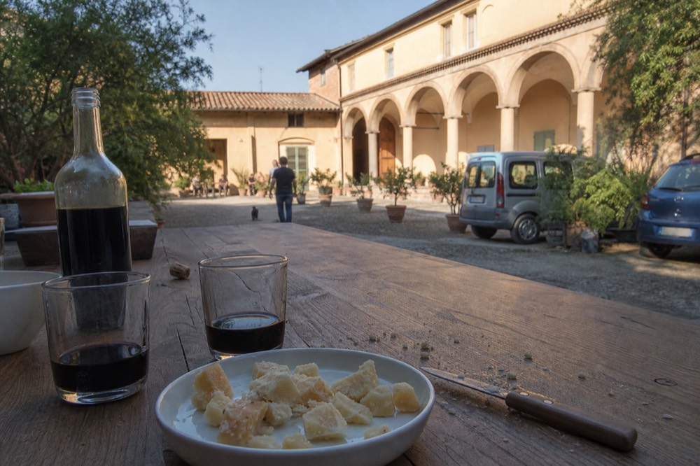 Two glasses of vinegar and a plate of cheese on a tasting table beside an open bottle