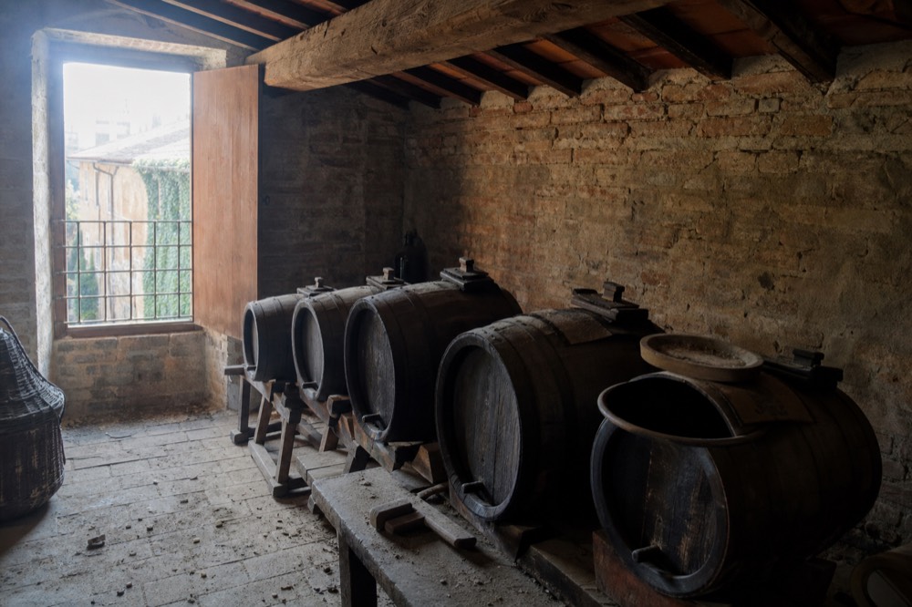 A row of wooden ageing barrels in a dim loft under a tiled roof
