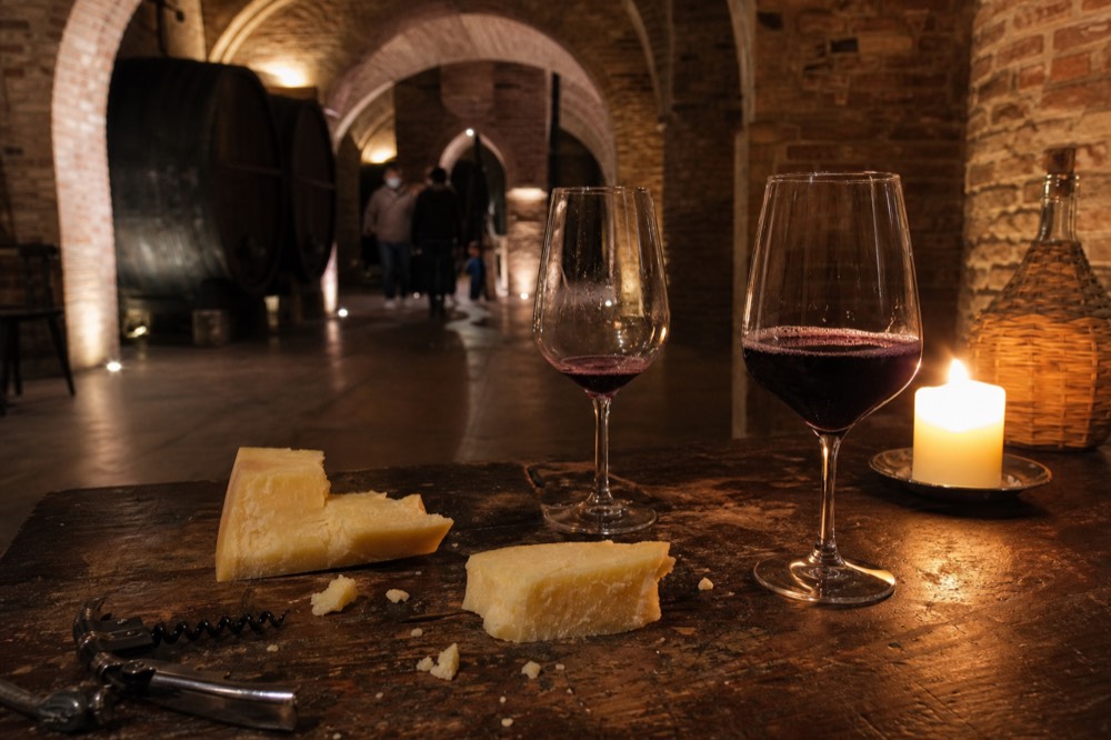 A plate of aged cheese wedges and glasses of red wine on a wooden counter