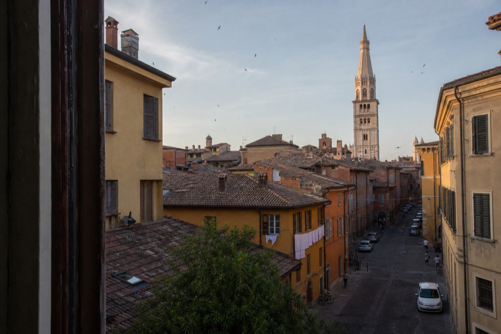 A quiet Italian street with an old tower rising above tiled rooftops