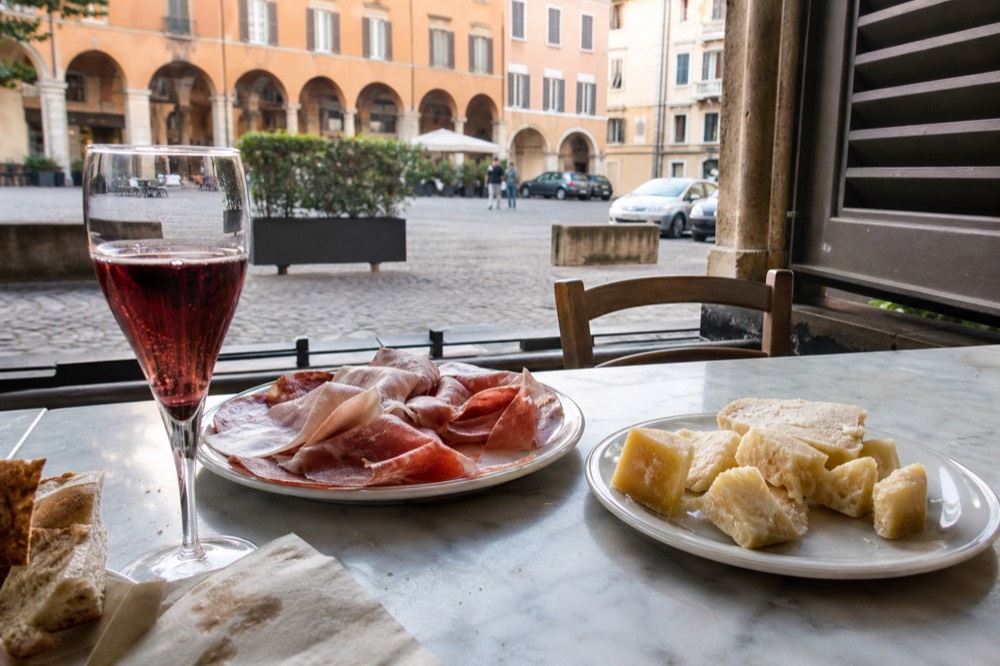 A plate of cured meats and aged cheese beside a glass of red sparkling wine