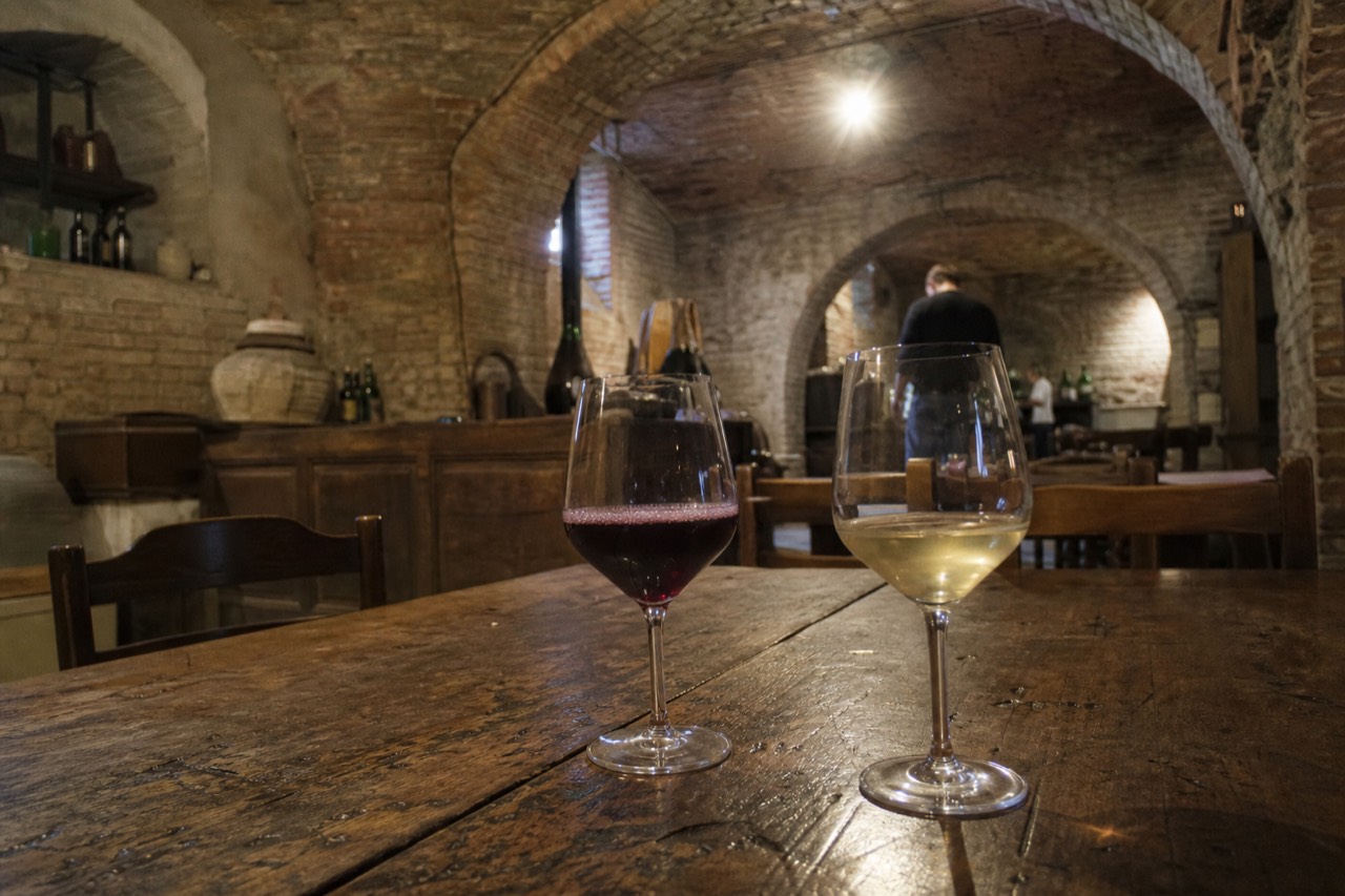 Two glasses of red and white sparkling wine on a wooden table in an Emilian cellar