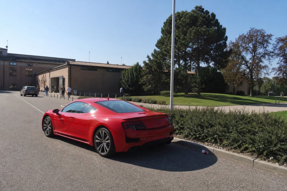 Red Ferrari parked outside the museum entrance in Maranello with a clear sky