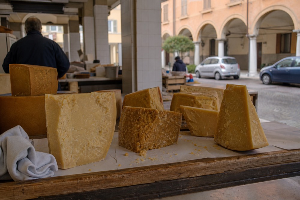 Wedges of Parmigiano Reggiano at different ages laid out on a wooden counter in a Modena cheese shop