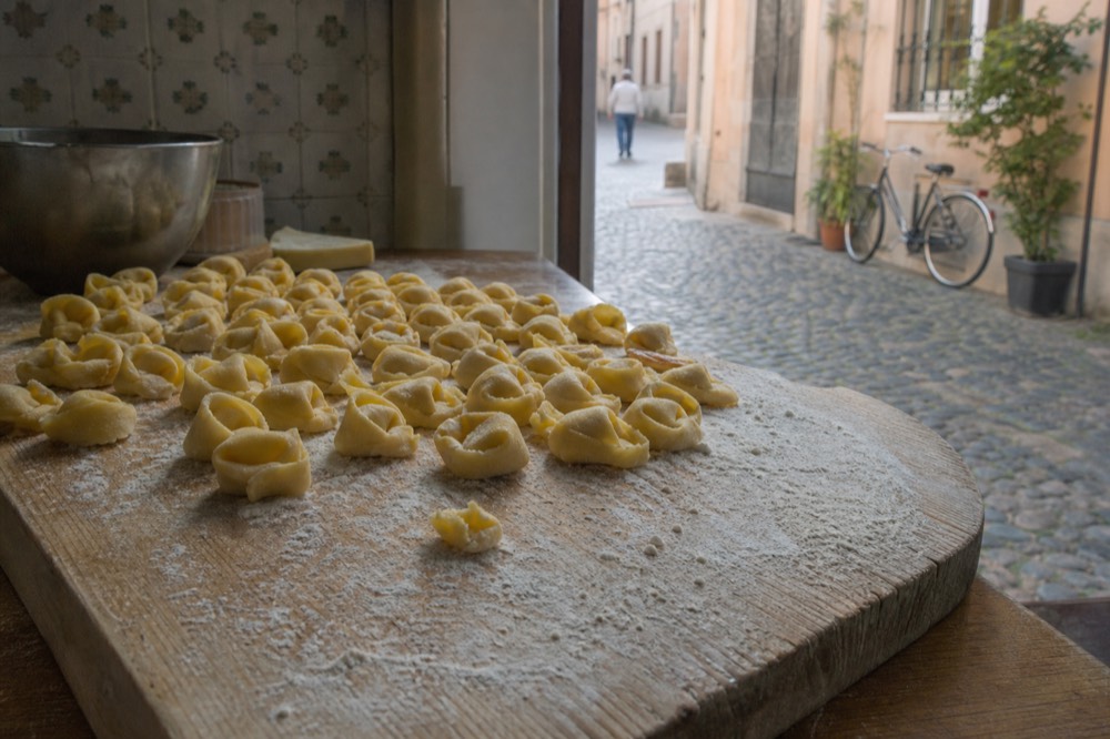 Small hand-folded tortellini pasta rings arranged in rows on a floured wooden board