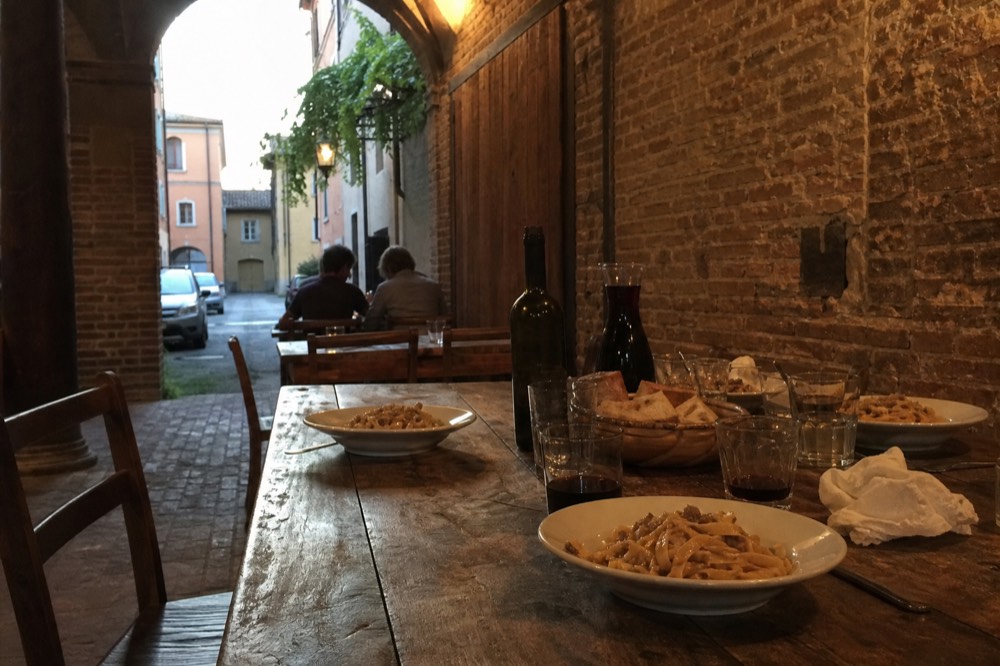 A long table set with plates of fresh ribbon pasta, bread and bottles of red wine in a rustic dining room