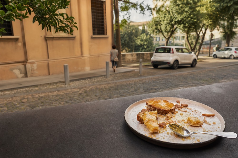 A broken lemon tart plated with scattered pastry shards on a dark surface