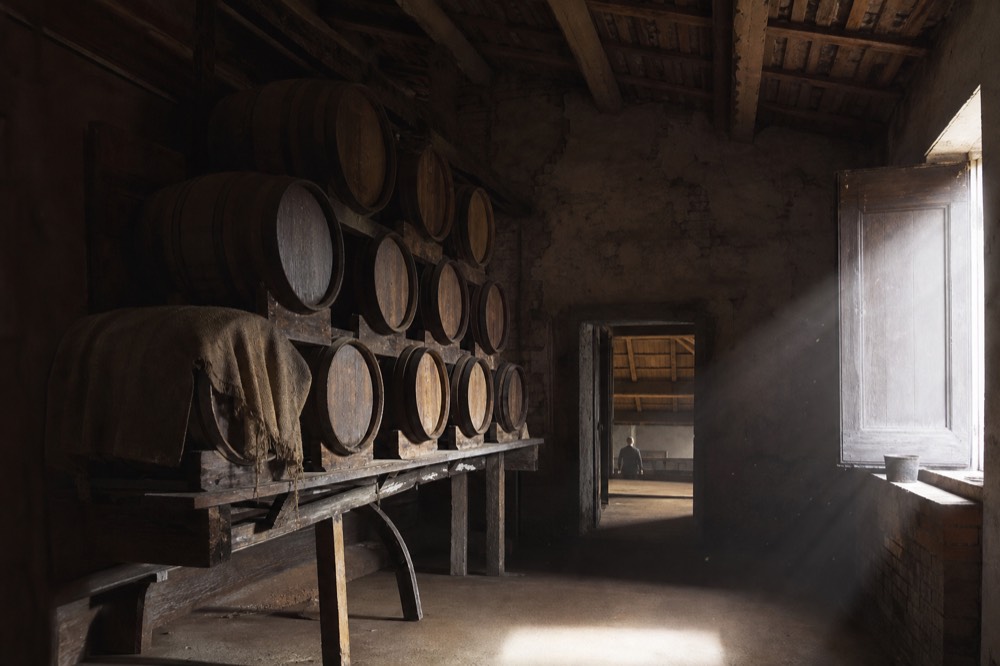 A row of small wooden barrels of different sizes stacked in a dim vinegar ageing attic