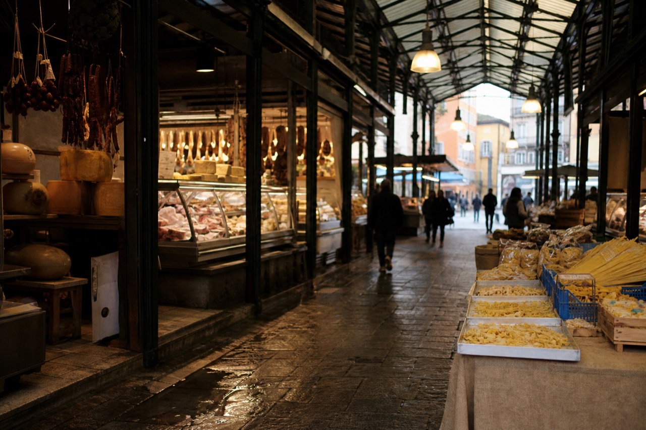 A covered food market hall with stalls of cheese, cured meats and fresh pasta under warm lights