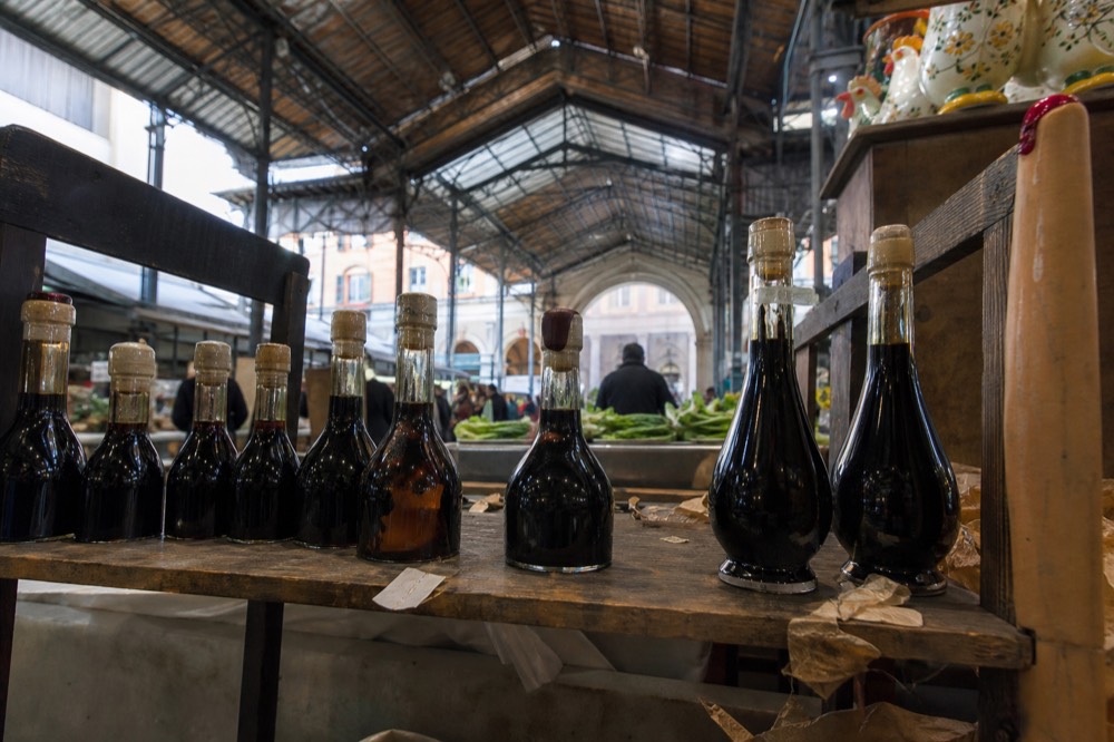Balsamic vinegar bottles lined up on a wooden market shelf with price tags