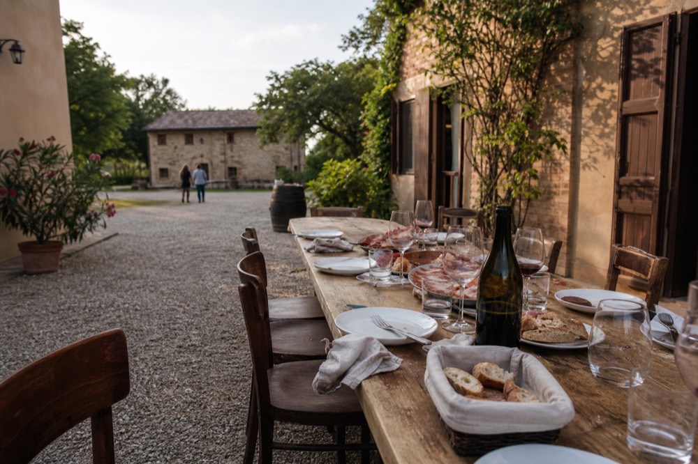 A long dining table set with wine glasses and plates of bread and cured meats in a rustic room