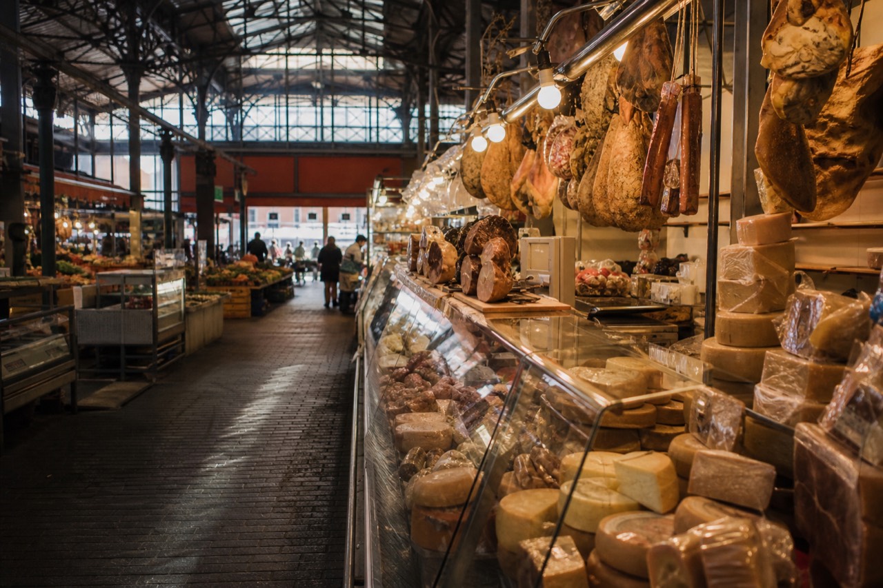 A covered market hall in Modena with stalls of cured meats, cheese wheels and fresh pasta under warm lights