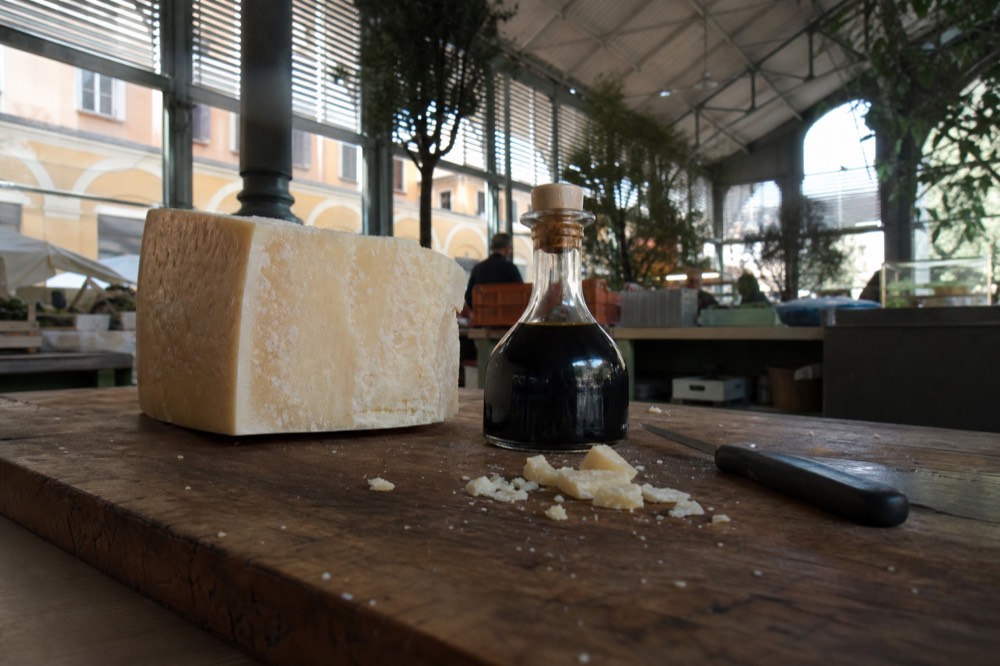 A wheel of aged cheese and a small bottle of dark vinegar on a wooden counter