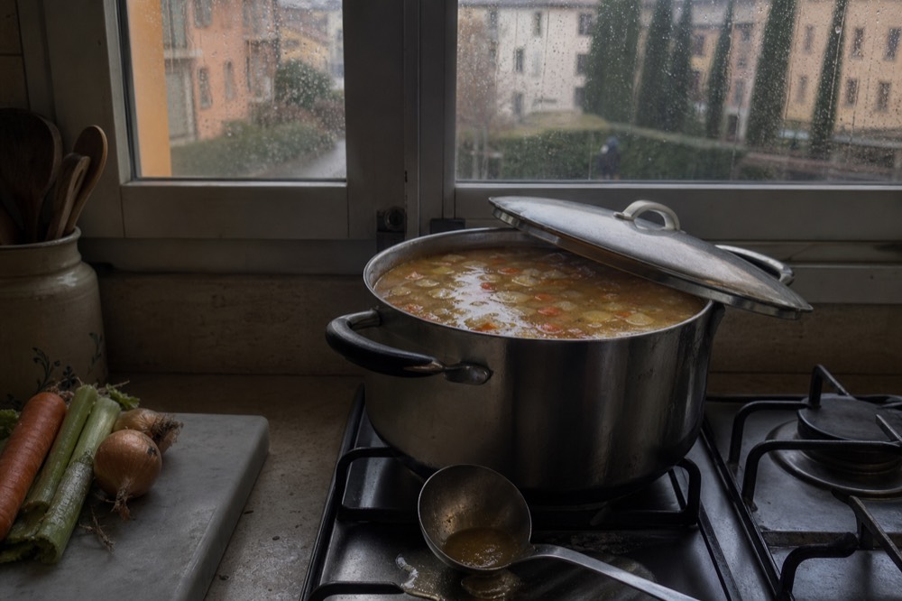 A pot of clear golden broth simmering with vegetables on a stove