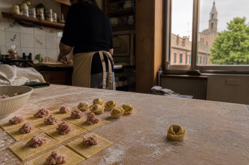 Hands folding small squares of pasta dough into tortellini on a floured wooden board