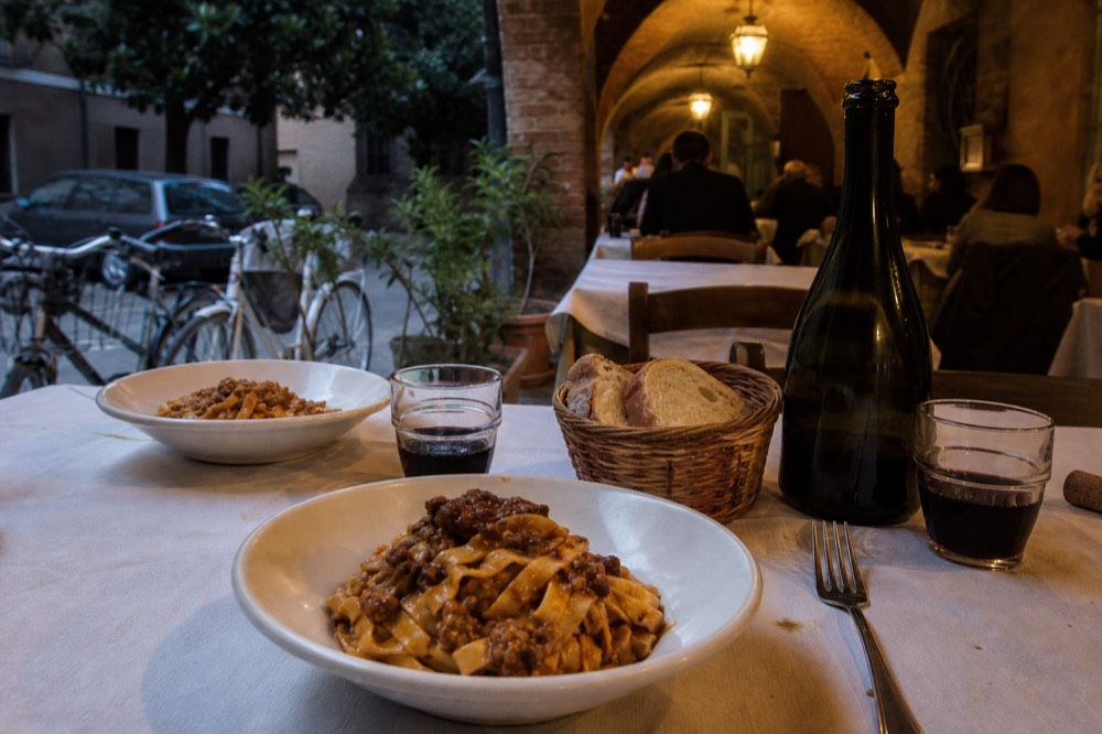 A Modena trattoria table set with bowls of pasta, bread and a bottle of Lambrusco