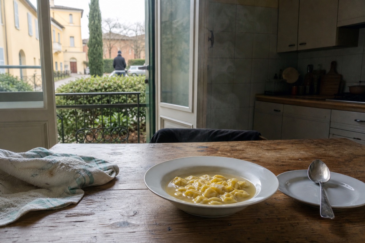 A bowl of tortellini in golden broth on a wooden table in a Modena kitchen