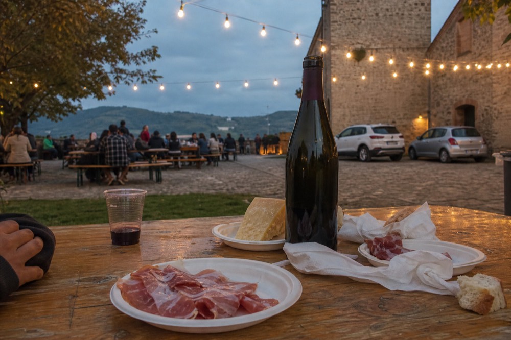 A table set with a bottle of Lambrusco, plates of cured meats and a wedge of aged cheese