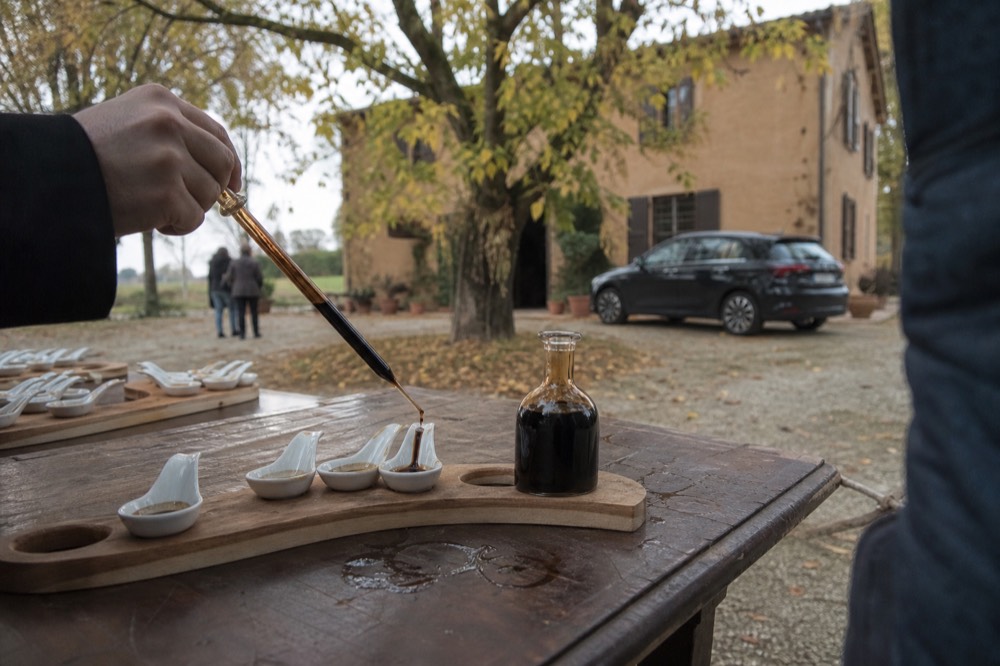A guide pouring a tiny measure of dark aged vinegar from a glass pipette into tasting spoons