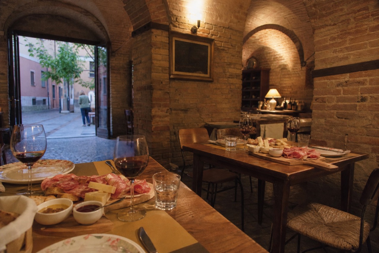 Two Italian city food tables set with cured meats, cheese and red wine in an old brick dining room