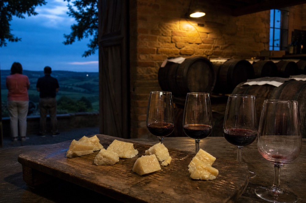 A tasting board of cheese cubes at different ages beside glasses of red wine