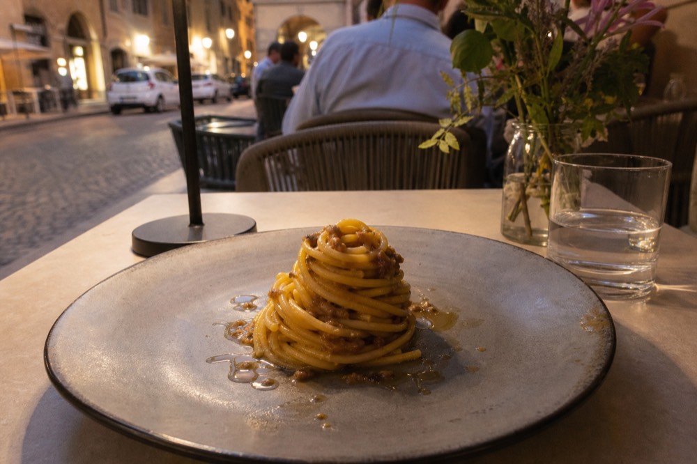 A modern plated dish with a spiral of pasta and a broth garnish
