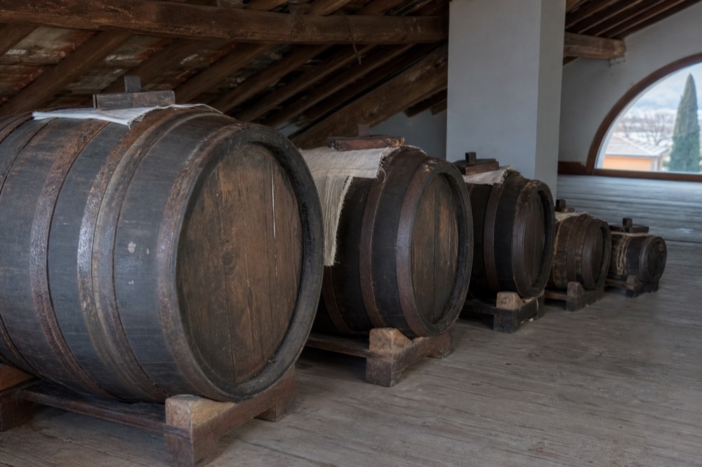 A row of ageing barrels of different sizes standing on a wooden attic floor