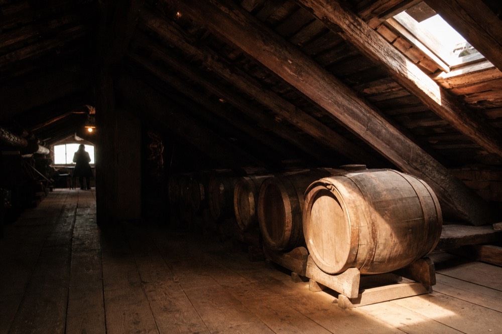 Small wooden barrels arranged in a descending row inside a dim acetaia loft