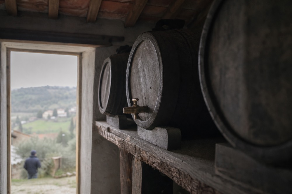 A wooden cask with a tap, set on a shelf in a historic acetaia, with labels indicating the vinegar's age.