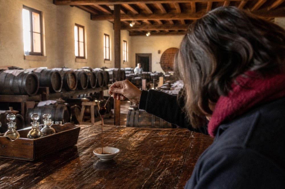 A guide pouring a few drops of thick balsamic vinegar onto a spoon during a tasting in a barrel loft.