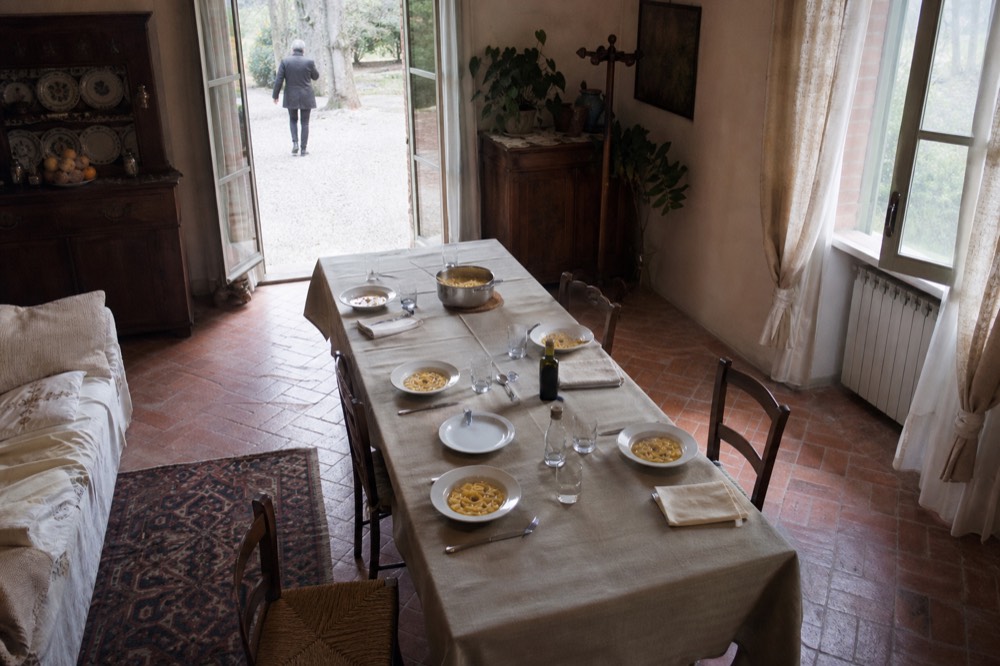 A table set with traditional Emilian dishes, including tortellini in brodo and a bottle of balsamic vinegar, in a villa dining room.