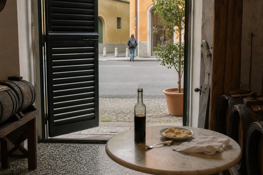 A small tasting table set with a bottle of balsamic vinegar, a spoon, and a plate of local cheese in a private acetaia room.